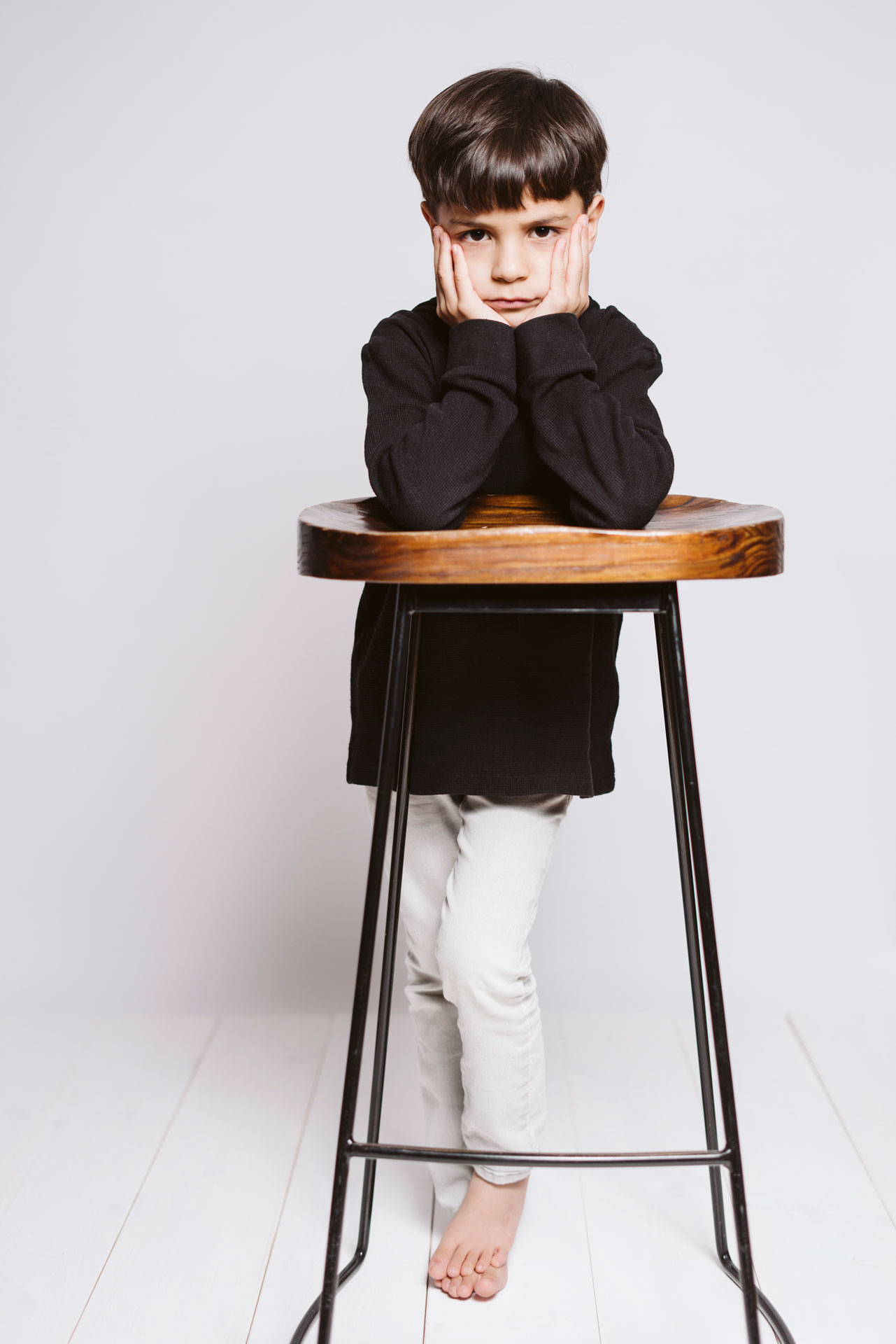 kindergartenfotografie-biszummondundwiederzurueck-duesseldorf Studioportrait eines Jungen, der beide Haende den Kopf stuetzend, ehrlich seinen Missmut ueber das fotografiert werden zeigt.