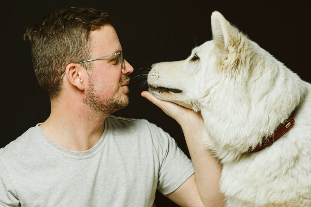 Junger Mann schaut seinem Hund in die Augen, waehrend er ihn festhält