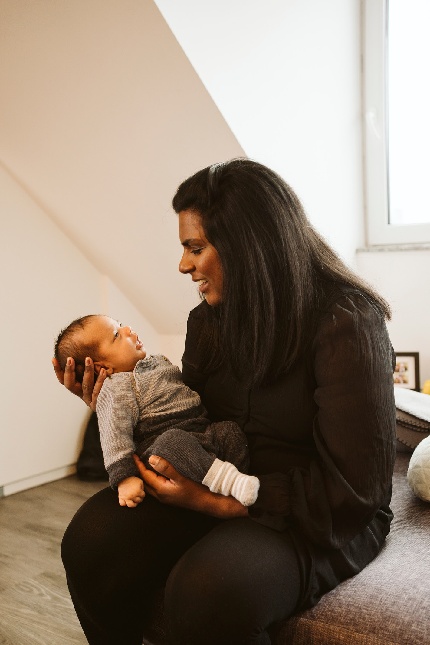 Mutter sitzt mit ihrem kleinen Baby im Arm am Fenster